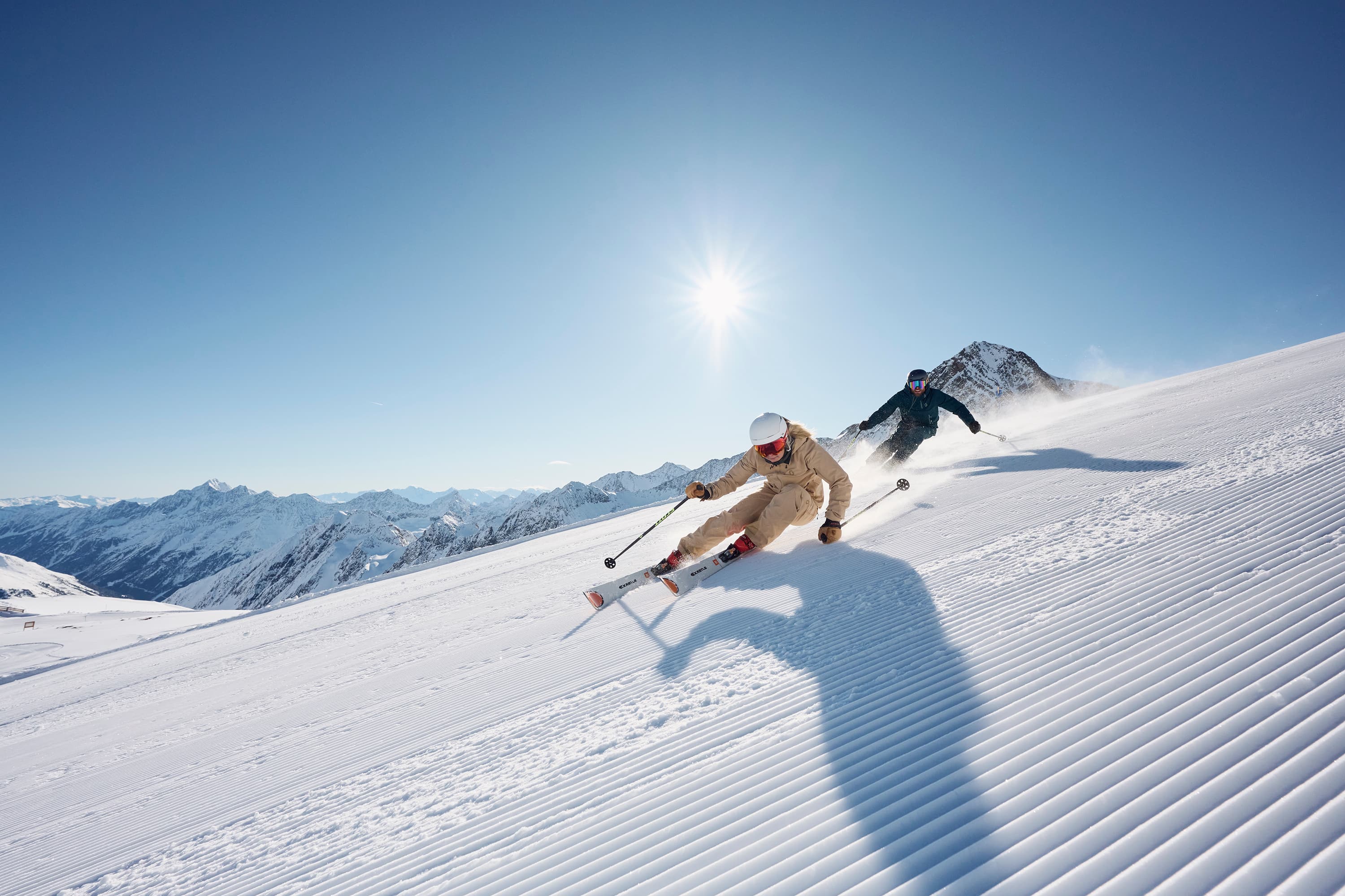 2 skiiers carving turns on ski slope under blue sky