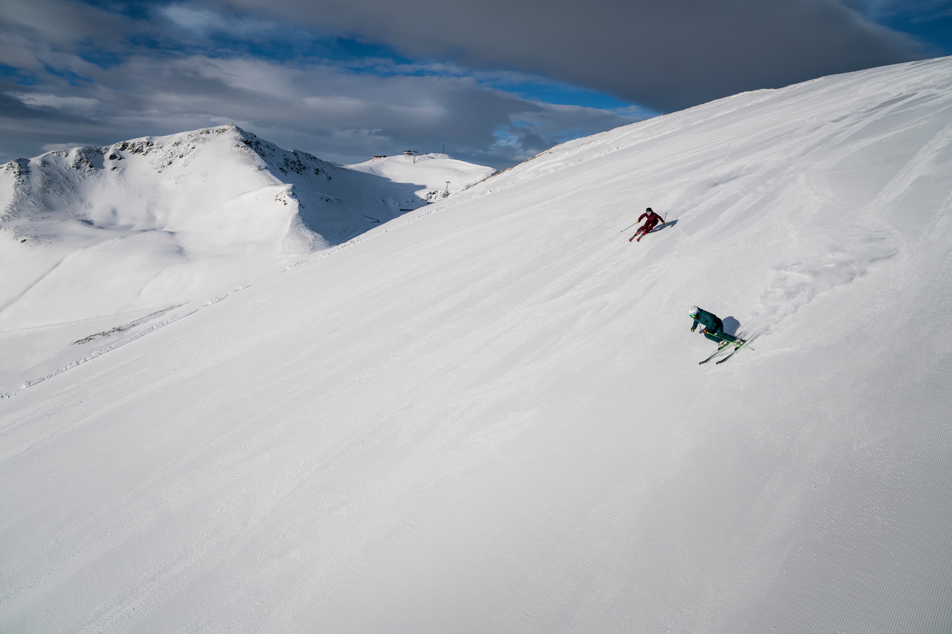 two skiiers skiing fast down wide open ski slope